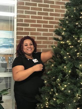 A student smiling at the camera while hanging an ornament on a Christmas tree