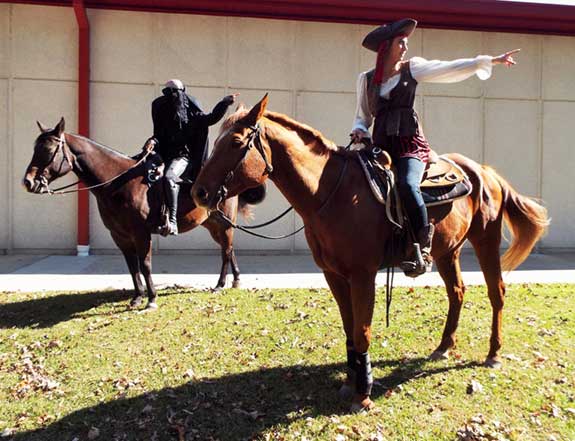 Two students riding horses on the college campus, wearing pirate Halloween costumes